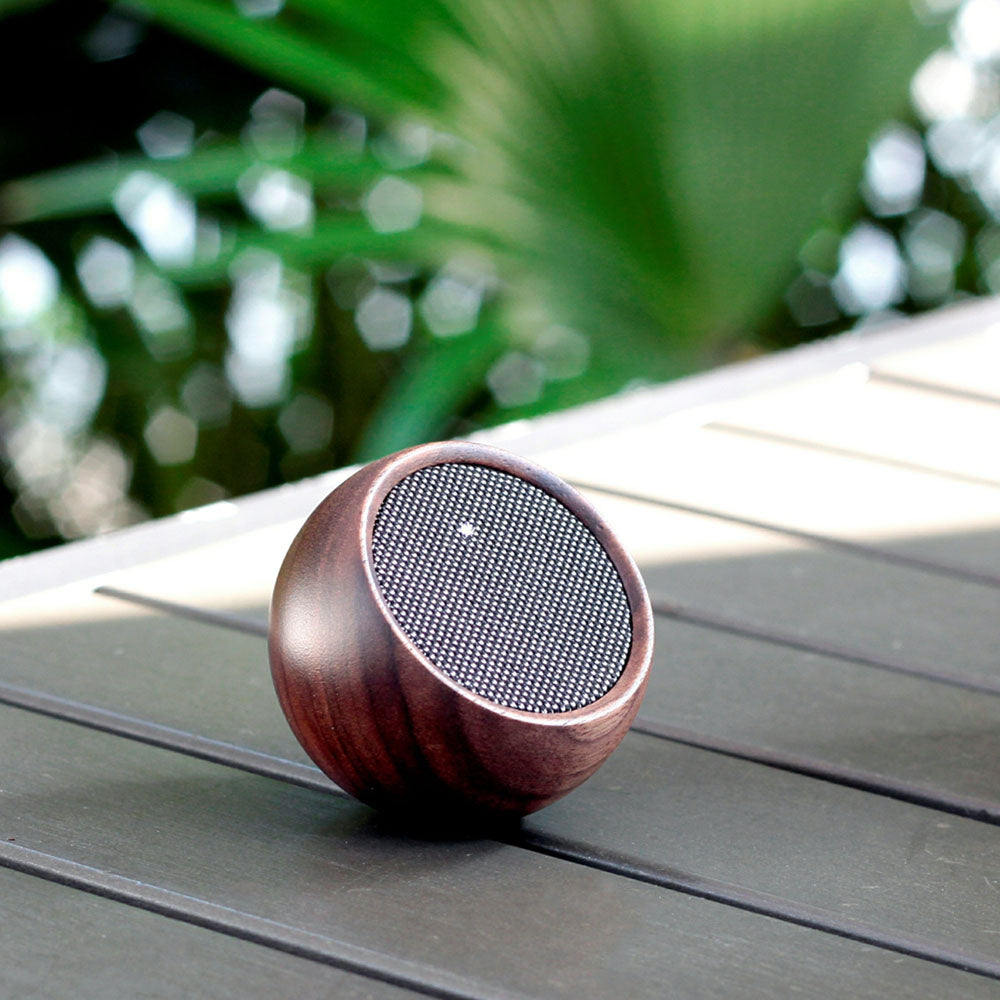 The Tumbler Selfie Speaker: Walnut displayed outdoors on a table.