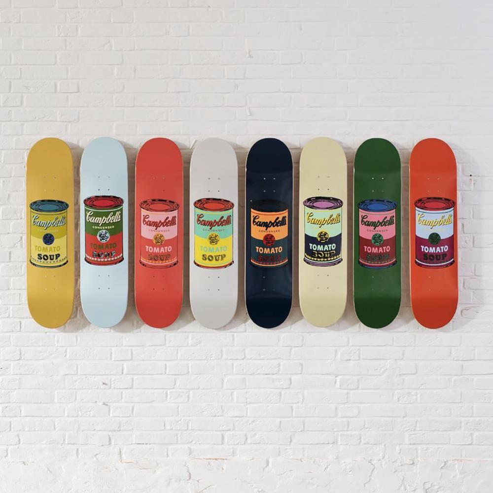 The eight skate decks from Warhol Soup Can Skateboards: Set of 8 lined up and mounted on a white brick wall.